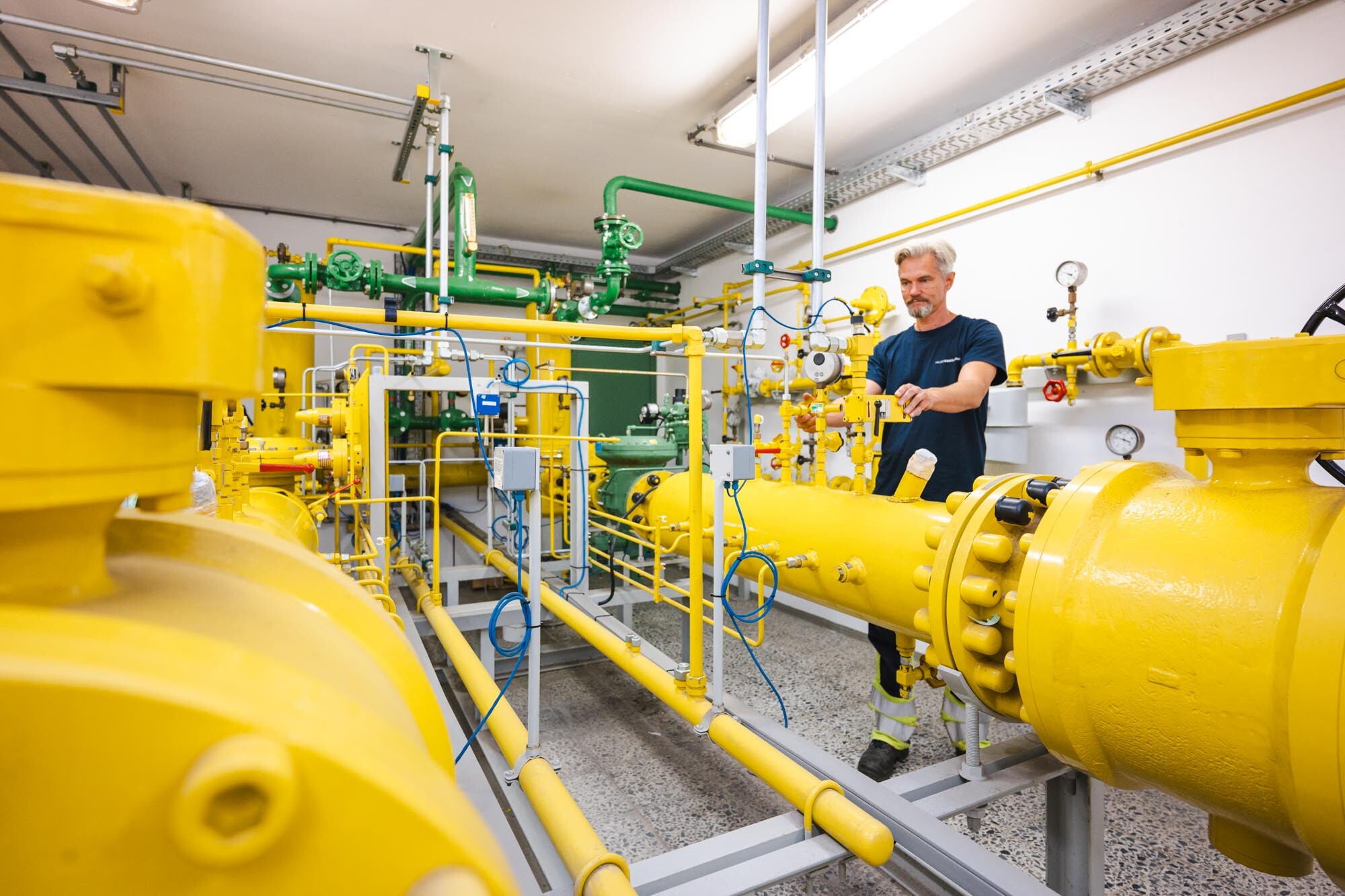 Im Vordergrund sieht man einige gelbe Rohre udnd Leitungen mit Messinstrumenten. Im Hintergrund steht ein Monteur der Halberstadtwerke an einem Rohr und misst etwas.