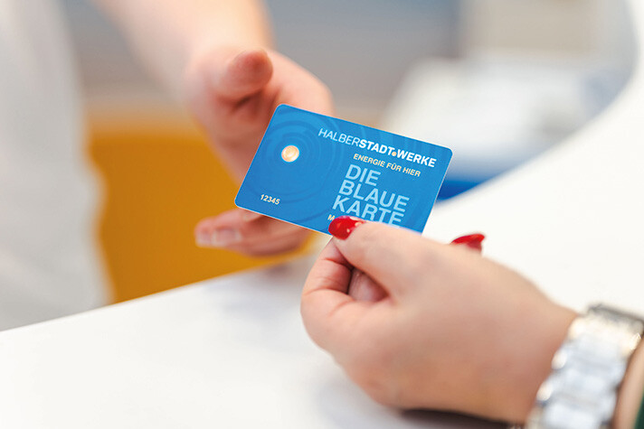 Die Blaue Karte wird symbolisch von einer Hand mit lackierten roten Fingernägeln an eine andere Hand übergeben.
